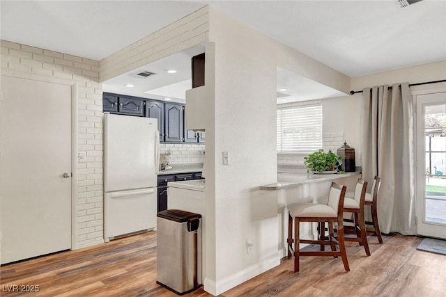 kitchen featuring visible vents, tasteful backsplash, light countertops, freestanding refrigerator, and light wood-style flooring
