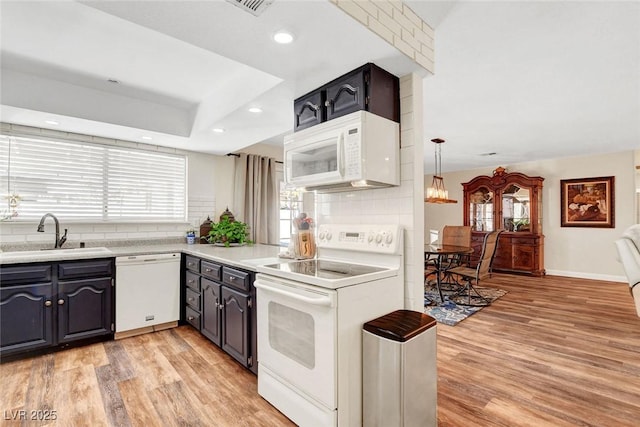 kitchen with tasteful backsplash, a sink, light countertops, light wood-style floors, and white appliances
