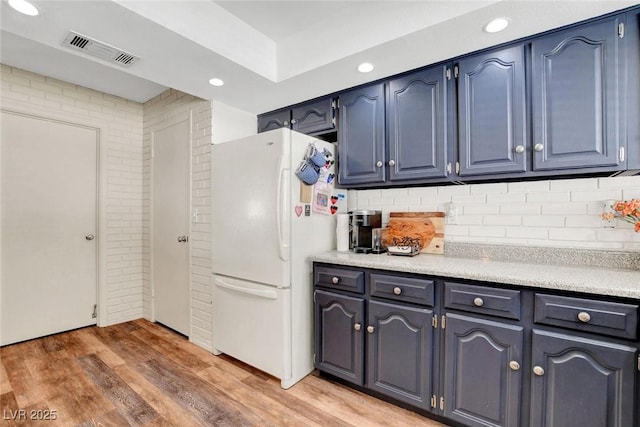 kitchen with light countertops, light wood-style flooring, freestanding refrigerator, decorative backsplash, and visible vents