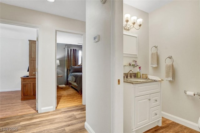 hallway with light wood-style floors, baseboards, a sink, and a chandelier
