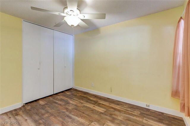 unfurnished bedroom with baseboards, a ceiling fan, wood finished floors, and a closet