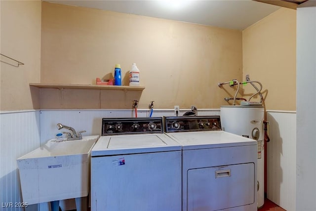 clothes washing area featuring laundry area, wainscoting, separate washer and dryer, a sink, and water heater