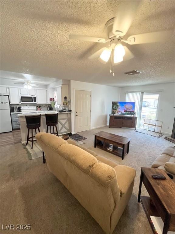 living area with visible vents, a ceiling fan, a textured ceiling, and carpet flooring