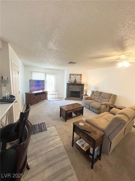 living area featuring a fireplace, carpet floors, a textured ceiling, a ceiling fan, and visible vents