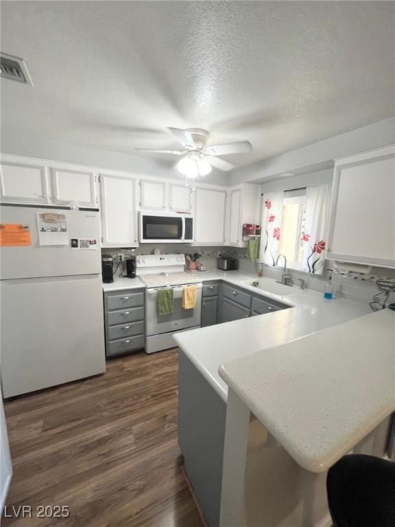 kitchen with a sink, light countertops, gray cabinetry, a peninsula, and white appliances