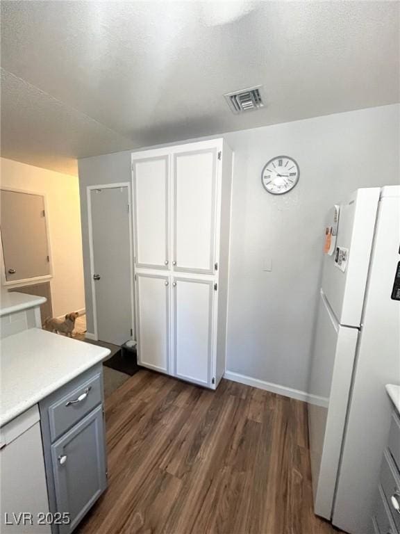 kitchen featuring light countertops, freestanding refrigerator, gray cabinetry, dark wood-type flooring, and visible vents
