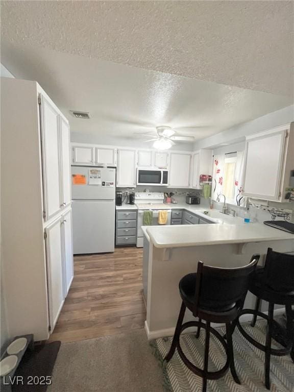 kitchen featuring a textured ceiling, visible vents, a sink, a peninsula, and white appliances