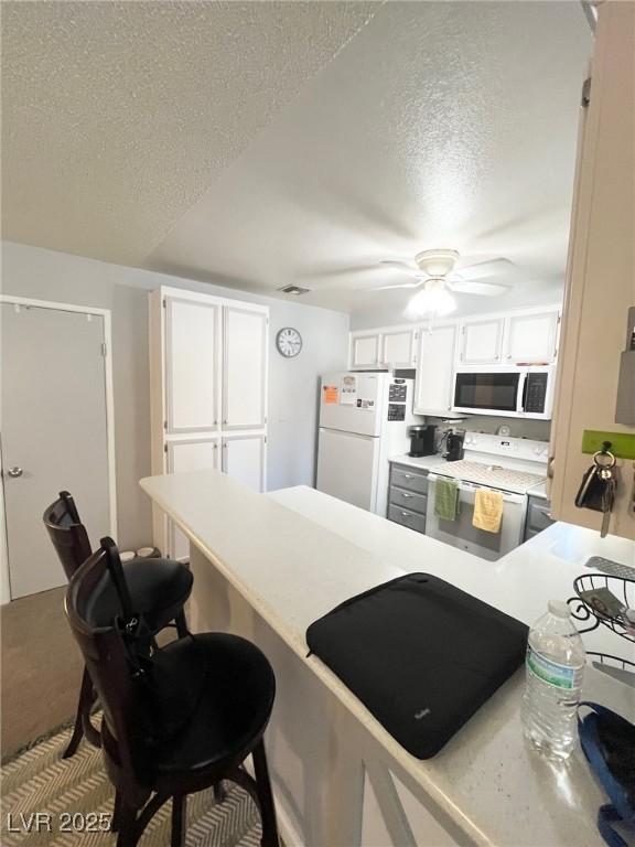 kitchen with white appliances, a textured ceiling, white cabinets, and a breakfast bar area