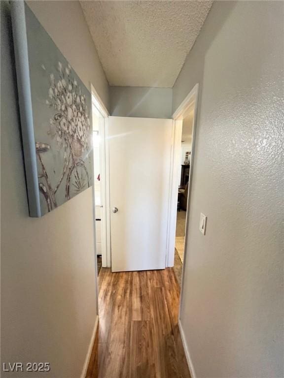 hallway with baseboards, a textured ceiling, and wood finished floors