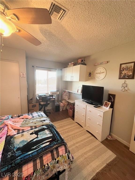 bedroom with ceiling fan, a textured ceiling, visible vents, and wood finished floors