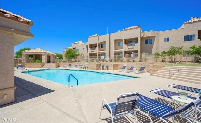 community pool featuring fence, a patio, and a residential view