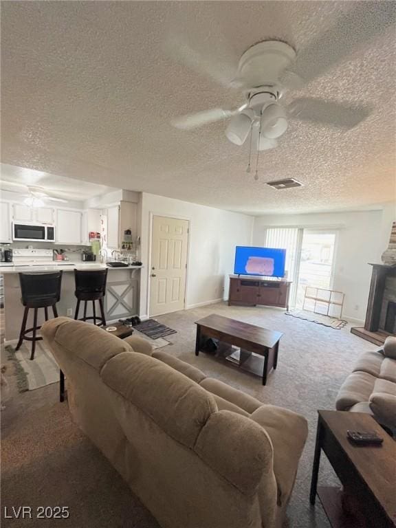 living area featuring carpet flooring, ceiling fan, a textured ceiling, baseboards, and visible vents