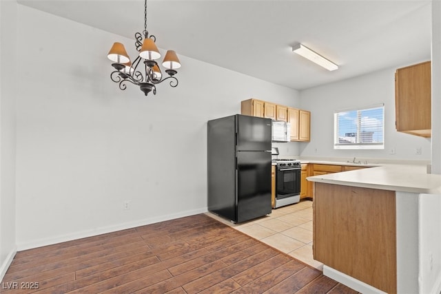 kitchen featuring freestanding refrigerator, a peninsula, light countertops, a chandelier, and gas stove