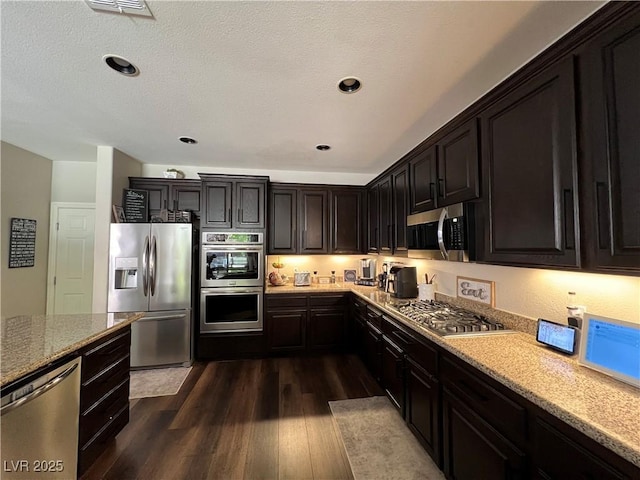 kitchen with stainless steel appliances, light stone countertops, and dark wood-style floors