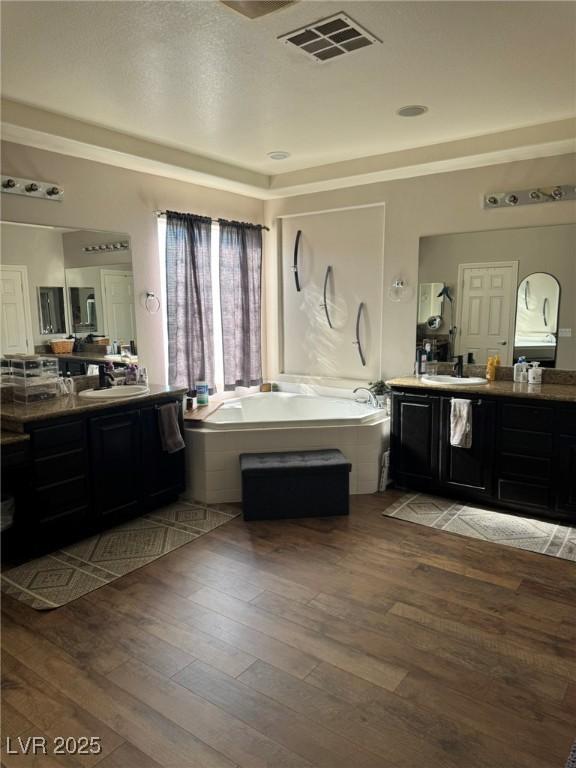 bathroom with a bath, visible vents, two vanities, and hardwood / wood-style flooring