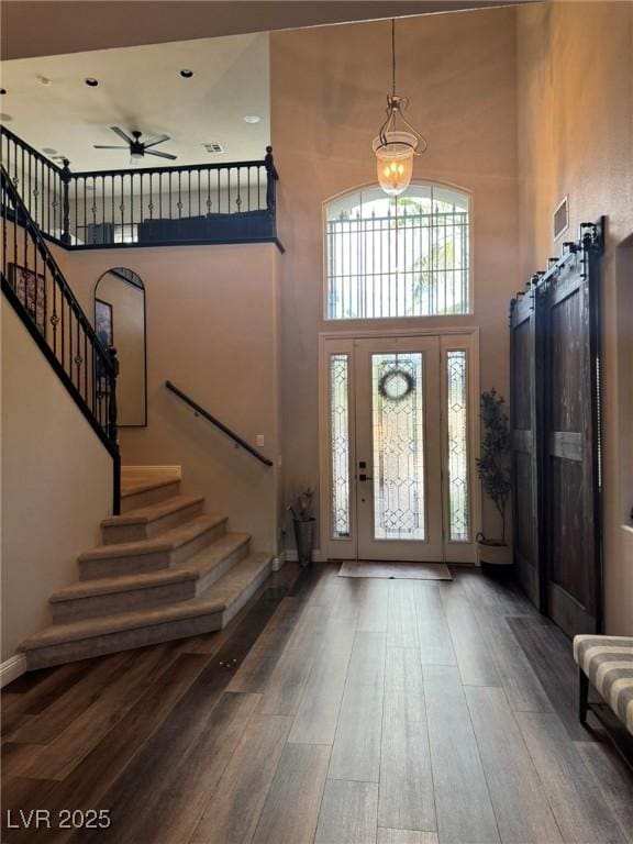 entrance foyer with stairs, a ceiling fan, a towering ceiling, visible vents, and hardwood / wood-style flooring