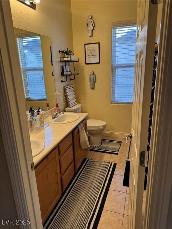 bathroom with double vanity, tile patterned flooring, a sink, baseboards, and toilet