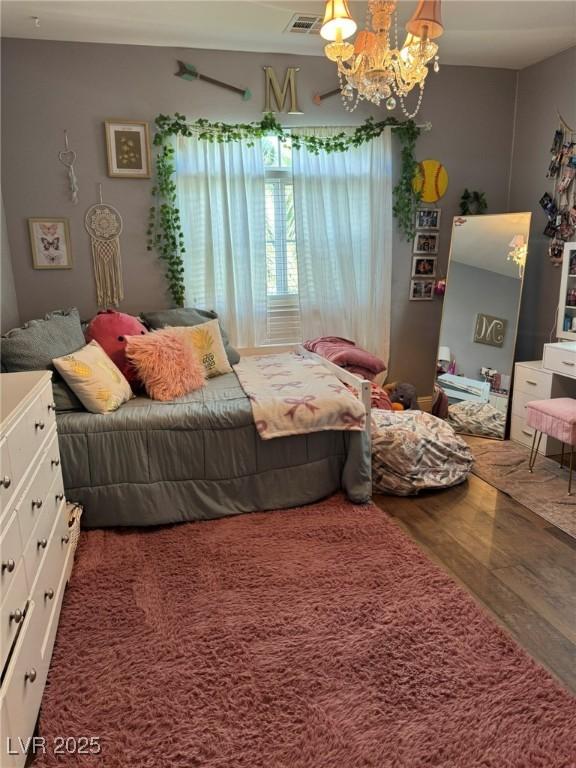 bedroom featuring visible vents, wood finished floors, and a notable chandelier