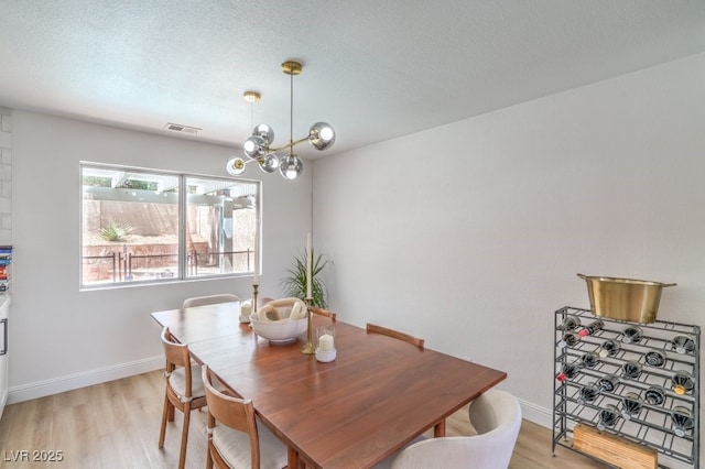dining space featuring an inviting chandelier, a textured ceiling, light wood-style flooring, baseboards, and visible vents