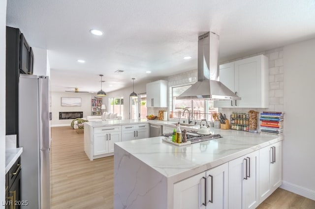 kitchen with appliances with stainless steel finishes, a sink, a peninsula, open floor plan, and island exhaust hood