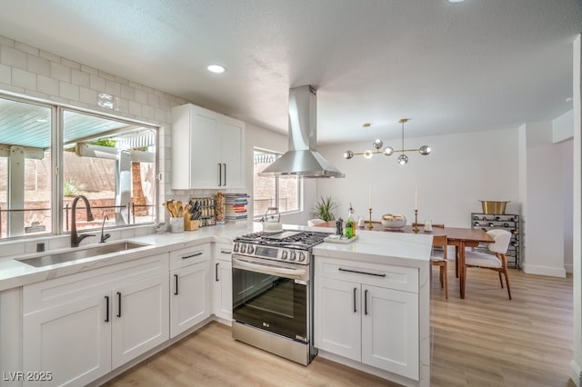 kitchen featuring a sink, stainless steel gas stove, a peninsula, white cabinetry, and island range hood