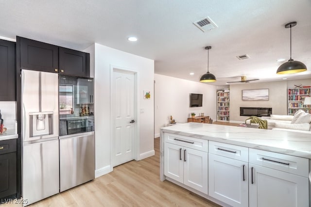 kitchen featuring visible vents, light wood-type flooring, light stone counters, and stainless steel fridge with ice dispenser
