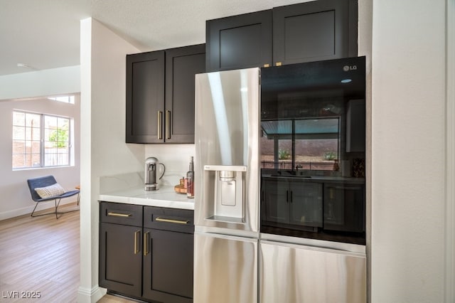 bar featuring baseboards, light wood-style flooring, and black refrigerator with ice dispenser