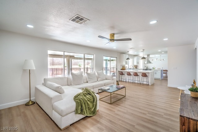 living room featuring visible vents, a ceiling fan, baseboards, and light wood-type flooring