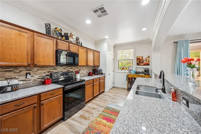kitchen with a sink, brown cabinetry, light wood-style flooring, visible vents, and black appliances