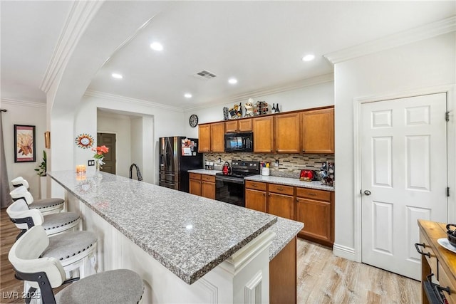 kitchen with a breakfast bar area, visible vents, light wood-type flooring, brown cabinets, and black appliances