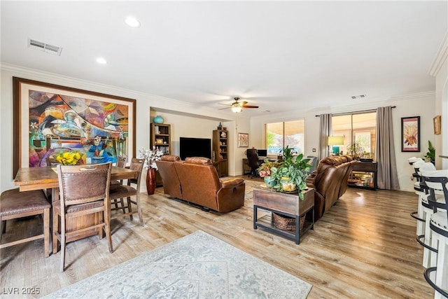 living area with crown molding, a ceiling fan, visible vents, and light wood-style flooring