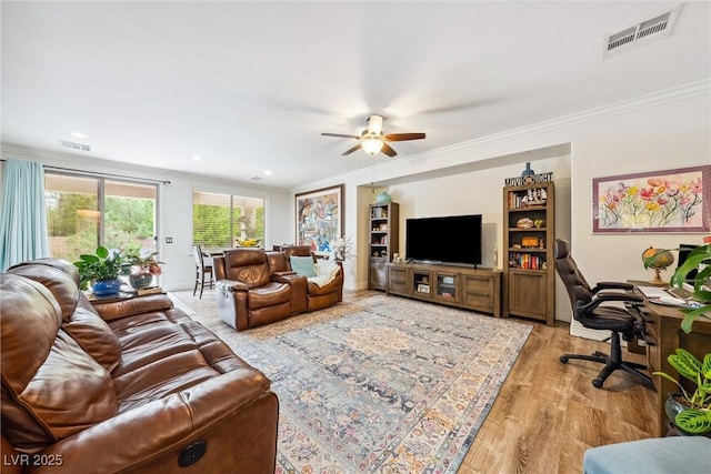 living room featuring visible vents, crown molding, light wood finished floors, and ceiling fan