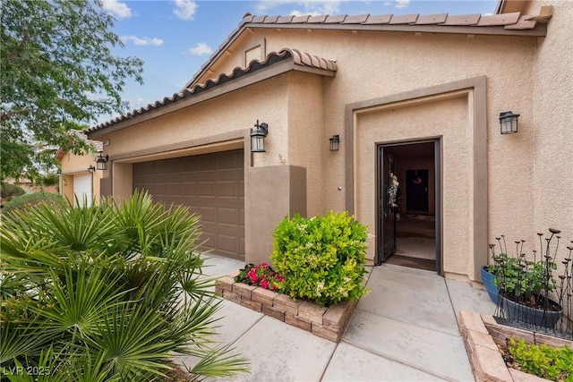 view of exterior entry with a garage and stucco siding
