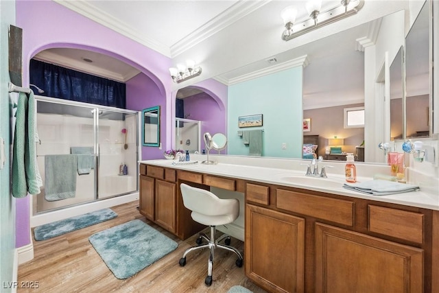 bathroom featuring ornamental molding, double vanity, wood finished floors, a sink, and a stall shower