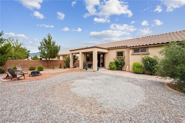 rear view of house with a tile roof, fence, a patio, a fire pit, and stucco siding