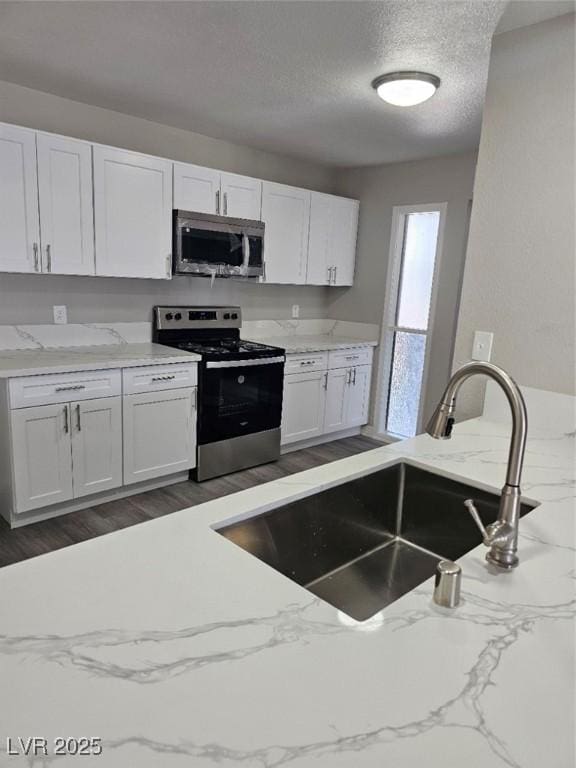 kitchen with white cabinets, appliances with stainless steel finishes, light stone counters, a sink, and a textured ceiling