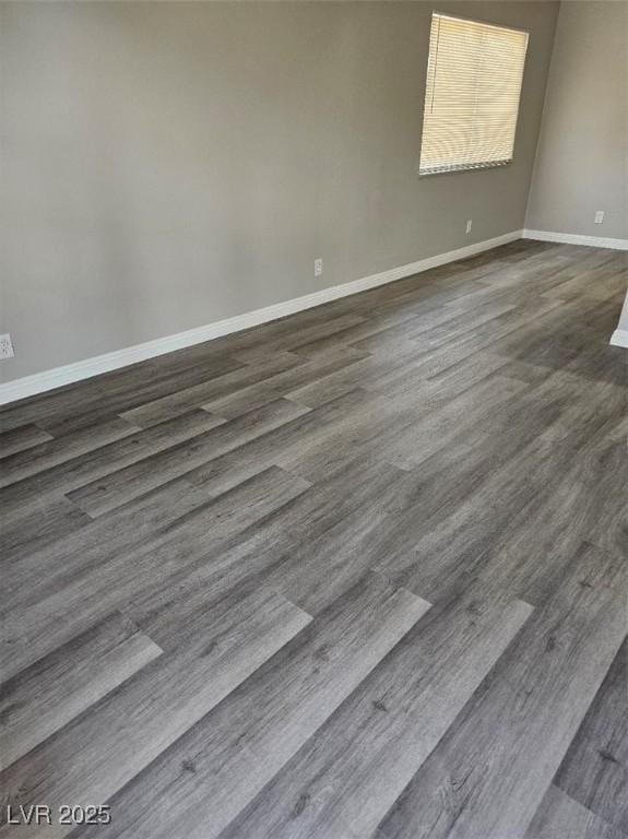 empty room featuring baseboards and dark wood-type flooring