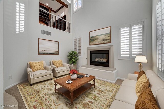 living room featuring a high ceiling, visible vents, a glass covered fireplace, and a wealth of natural light