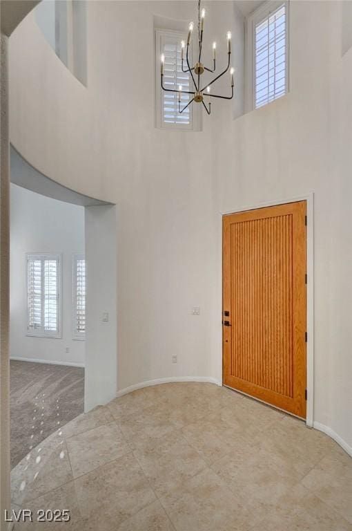foyer entrance featuring a high ceiling, a chandelier, and baseboards