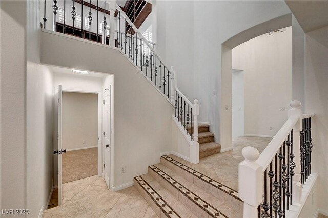 stairway featuring arched walkways, tile patterned flooring, and a towering ceiling