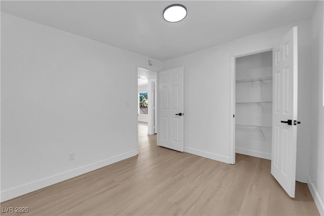 unfurnished bedroom with baseboards, light wood finished floors, a spacious closet, and a closet