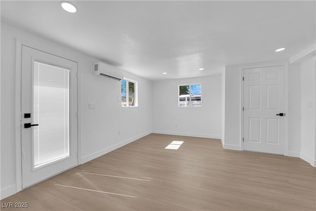 empty room featuring recessed lighting, baseboards, a wall mounted AC, and light wood finished floors