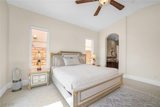 bedroom with baseboards, arched walkways, ensuite bathroom, and lofted ceiling