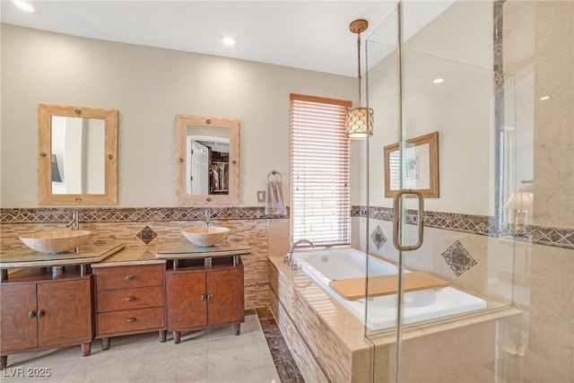 full bath with double vanity, a sink, a garden tub, and a stall shower