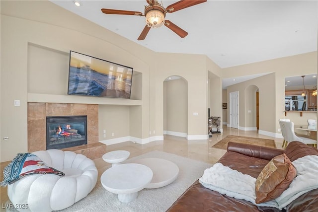 living area featuring ceiling fan, arched walkways, a tiled fireplace, recessed lighting, and baseboards