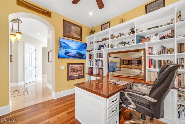office area featuring baseboards, arched walkways, light wood finished floors, and ceiling fan