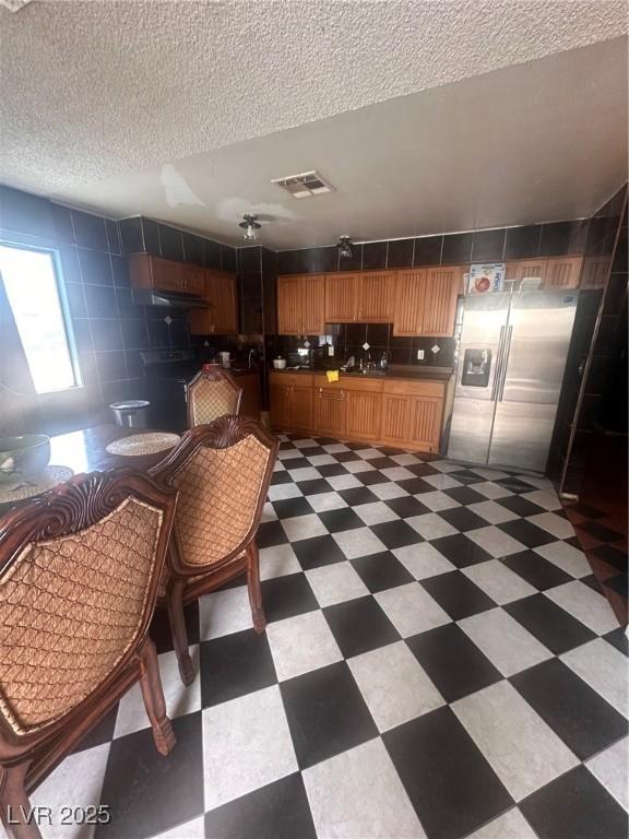 kitchen featuring dark countertops, stainless steel fridge, a textured ceiling, light floors, and visible vents