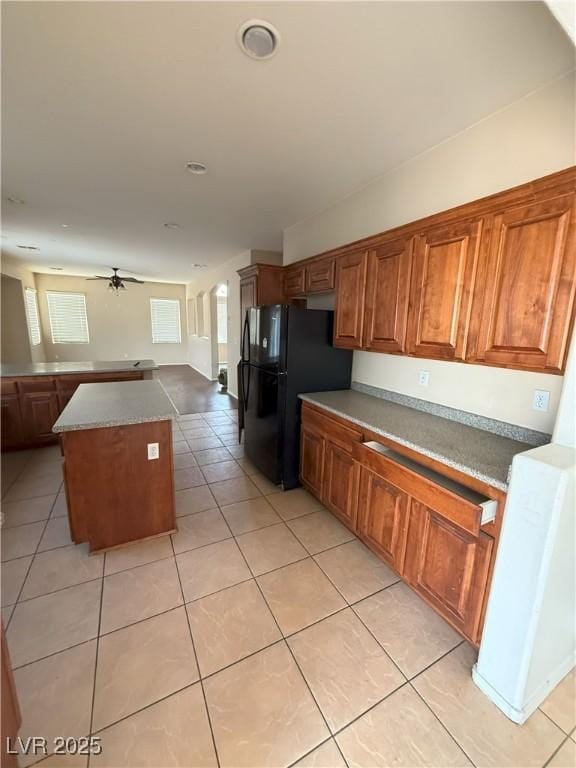 kitchen featuring freestanding refrigerator, brown cabinets, ceiling fan, and light tile patterned floors