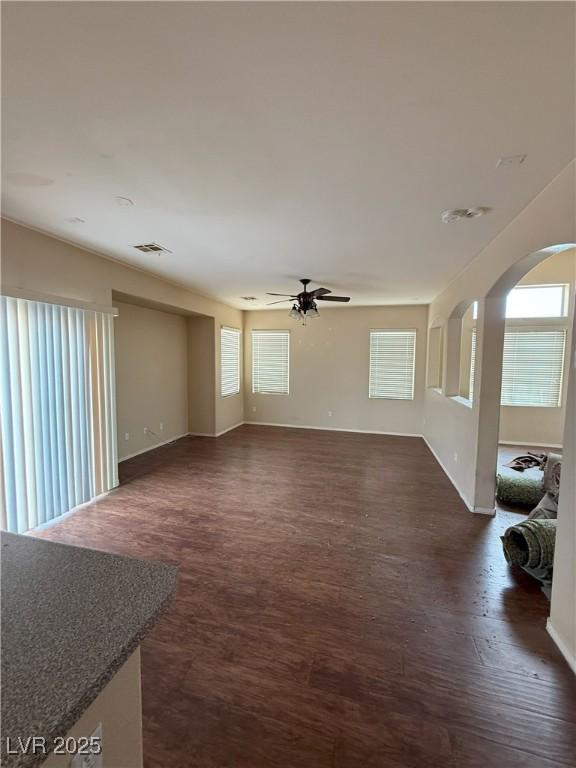 unfurnished living room featuring baseboards, arched walkways, dark wood finished floors, and ceiling fan