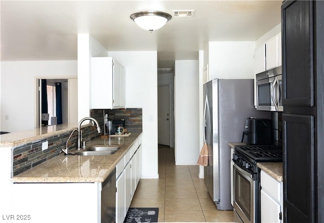 kitchen featuring visible vents, a peninsula, tasteful backsplash, a sink, and stainless steel appliances